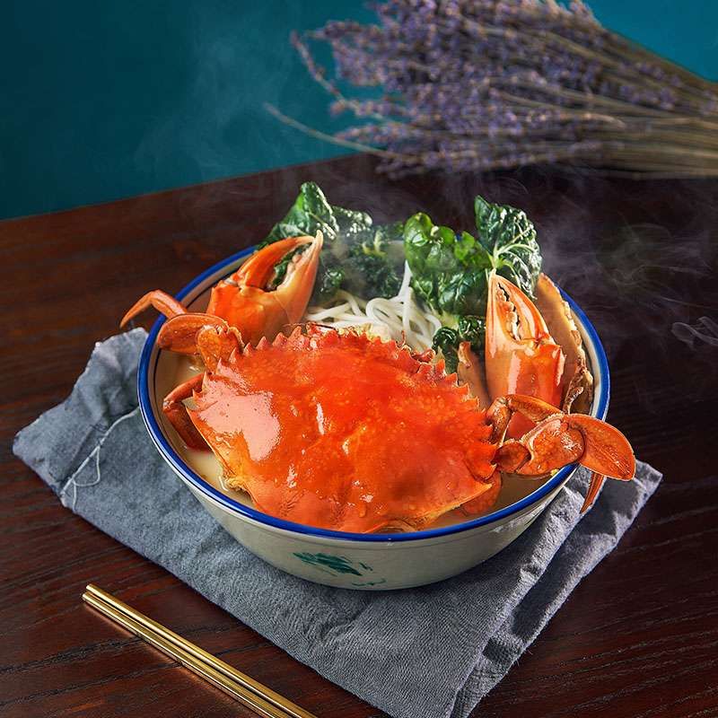 A steaming bowl of crab bee hoon soup with a whole crab, bee hoon and greens, photographed square for the kiosk menu