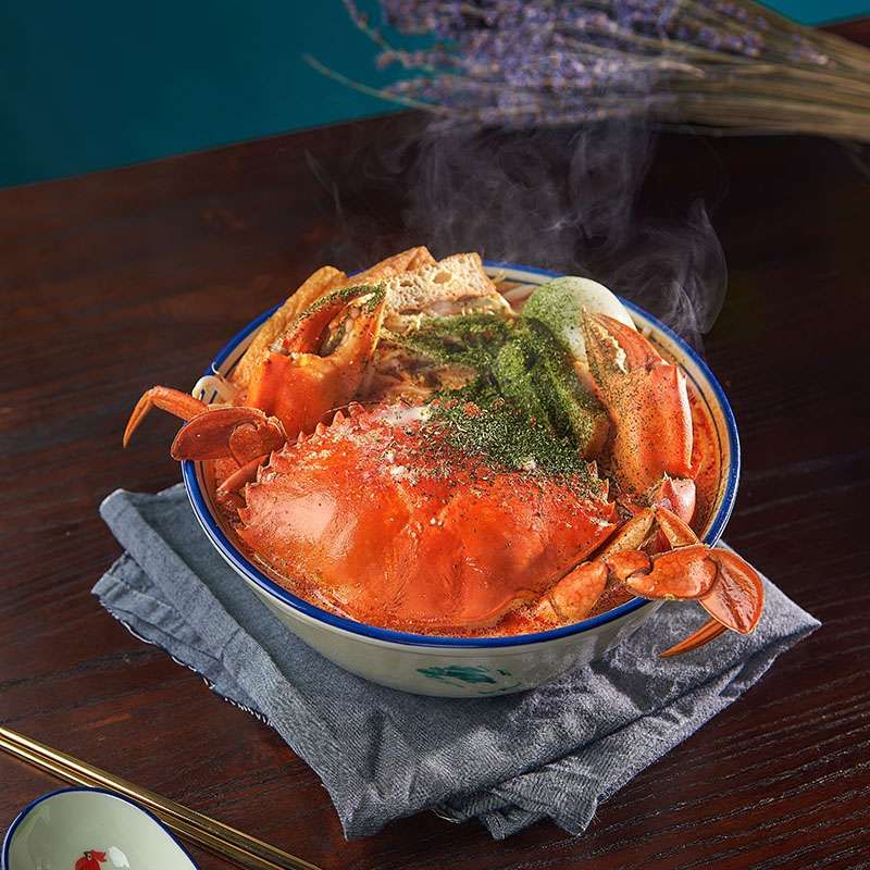 A bowl of crab laksa bee hoon with a whole crab and a green herb topping, photographed square for the AMK Hub kiosk menu